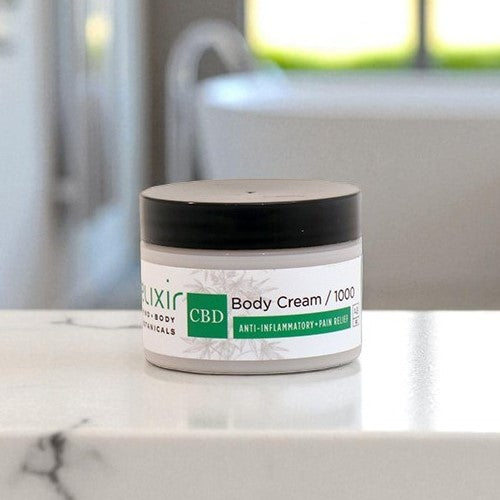 Jar of Elixir Mind Body Botanicals 1000 mg CBD Cream in a white marble bathroom