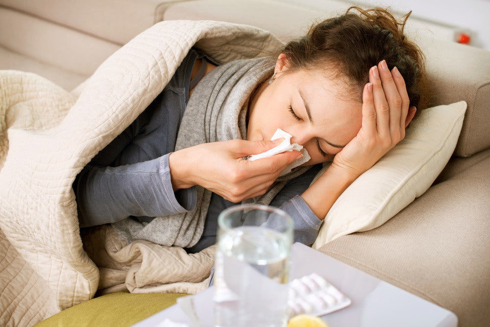 Sick woman lying on her couch blowing her nose with cold medicine on the table next to her