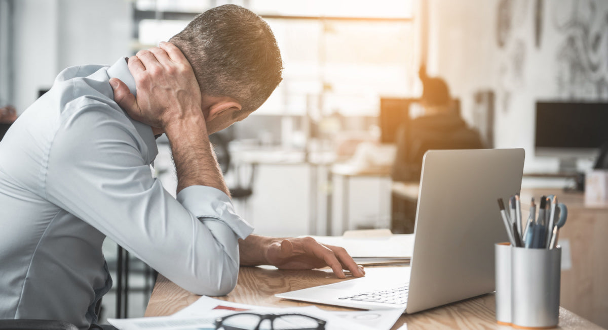 Man at work with laptop suffering from pain in the neck he is trying to massage