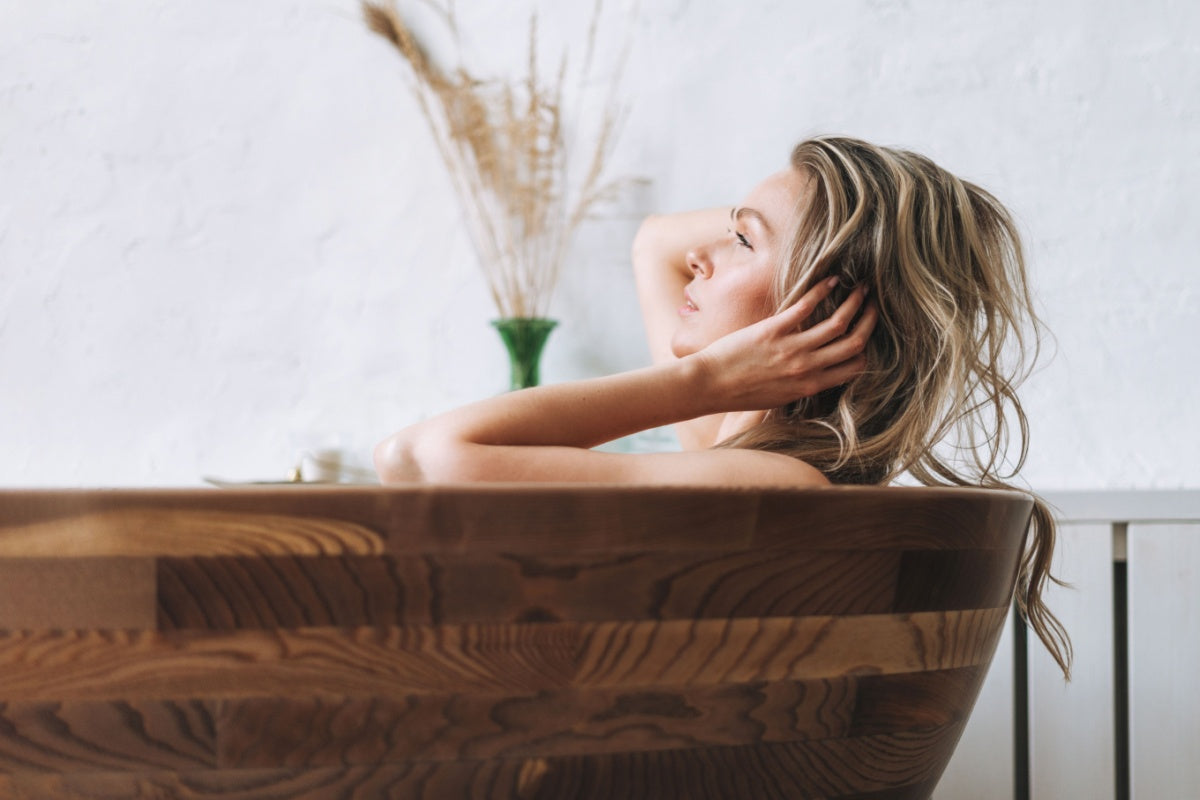 Woman soaking in modern teak tub using Elixir Mind Body Botanicals bath products