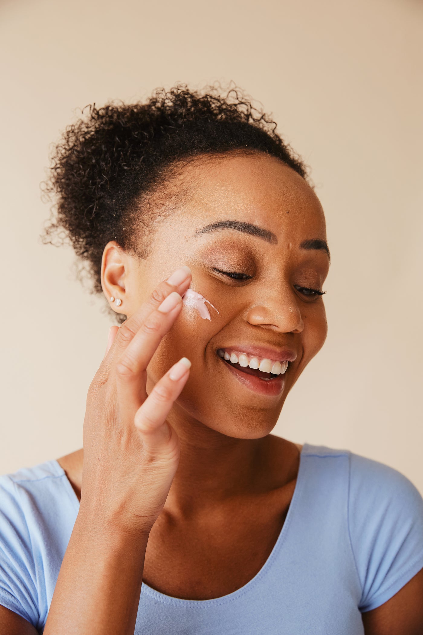 Photo of a woman applying face cream to her cheek.