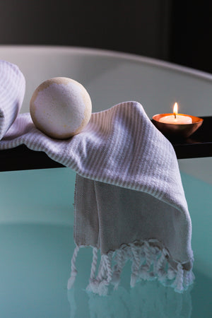 Photo of a bath bomb on a towel and a lit candle over a bathtub filled with water.