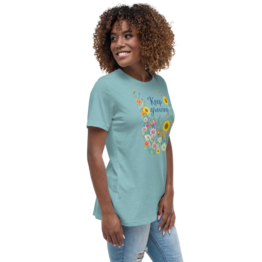 Right side view of a smiling woman wearing her relaxed heather blue short-sleeved t-shirt with a colorful, floral design on the front that says "Keep Growing."