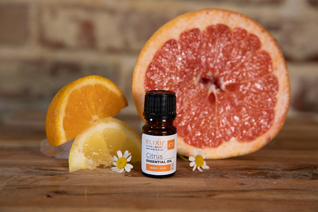 Elixir Mind Body Botanicals Citrus Essential Oil with slices of lemon, orange, and grapefruit on a butcher block countertop
