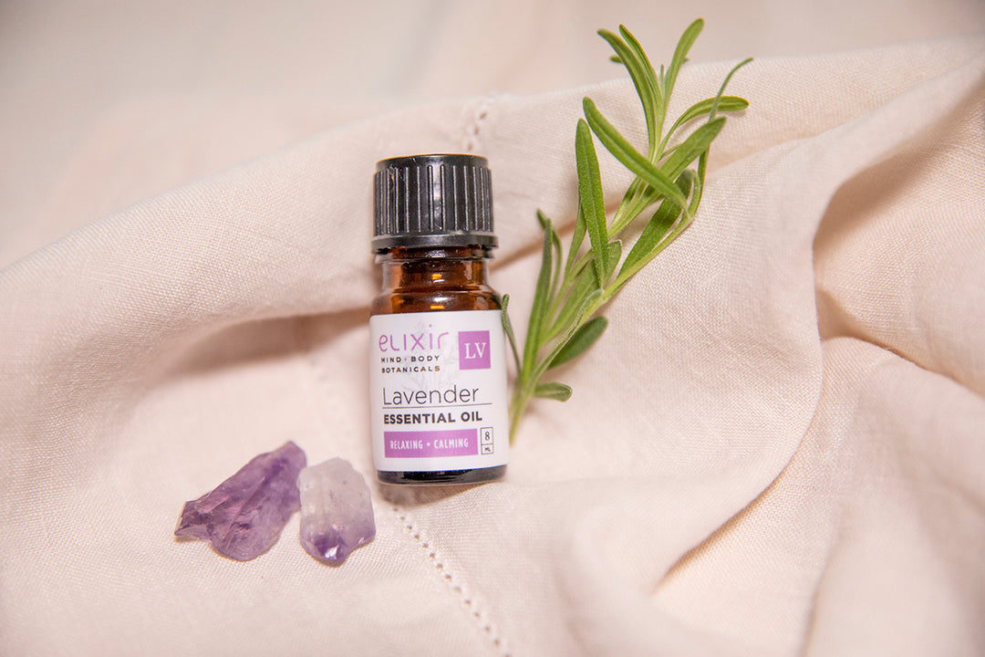 Elixir Mind Body Botanicals Lavender Essential Oil on Linen next to a lavender sprig and crystals