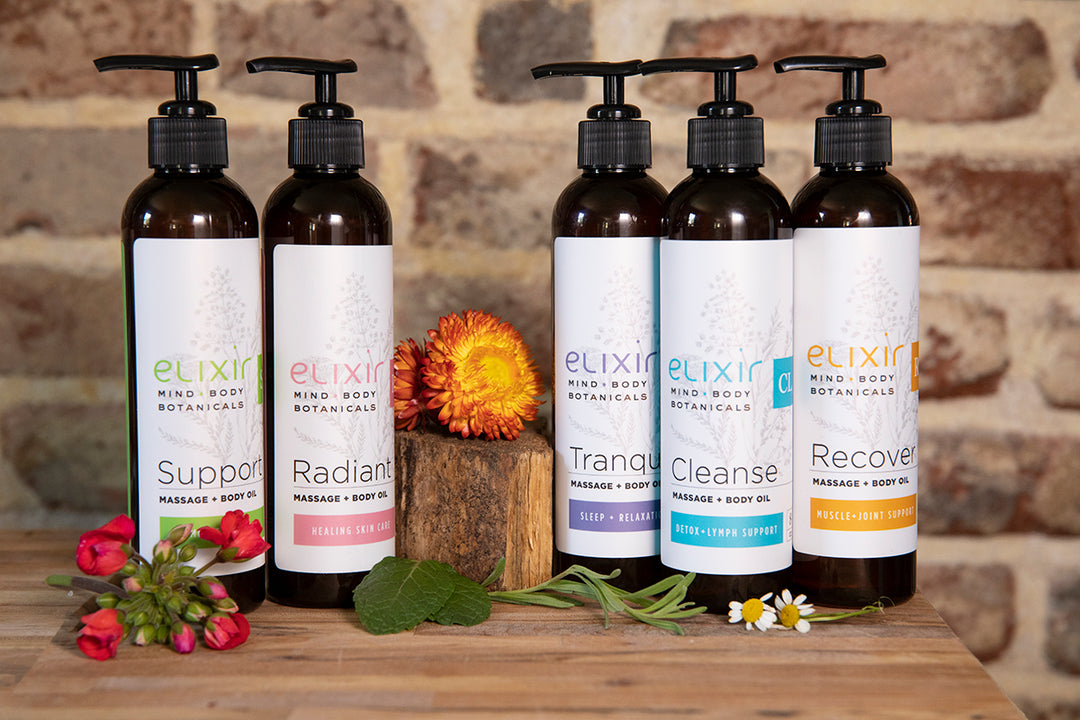 Elixir Mind Body Botanicals Massage and Body Oils in 5 scents, Support, Radiant, Tranquility, Cleanse, and Recover sitting on a butcher block counter top in front of a brick background