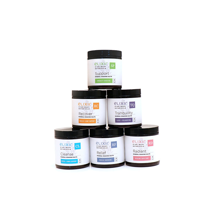 A stack of six jars of Elixir Mind Body Botanicals Mineral Soaking Salts with various labels indicating different product blends such as Relief, Recover, Support, Cleanse, Tranquility, and Radiant.