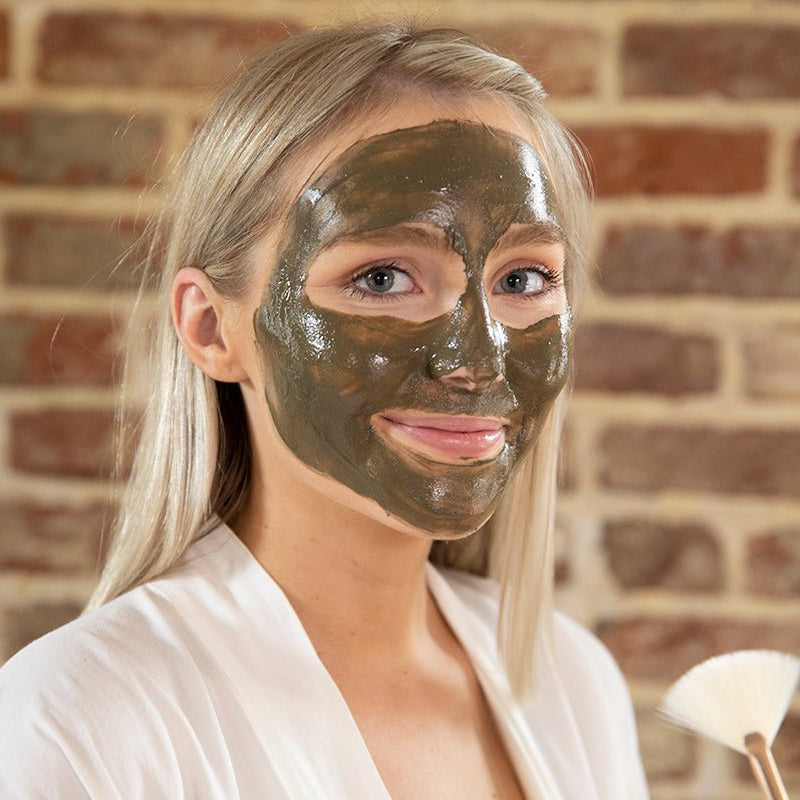 Woman using the Elixir Mind Body Botanicals Mineral Mud Mask on her face for clearer, softer skin. Elixir Mind Body Boutique